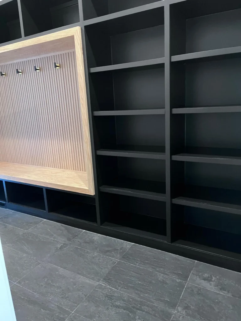A custom mudroom built-in featuring a clean wood-slatted bench, brass hooks, and dust-free black storage shelving maintained by L&V Cleaning.