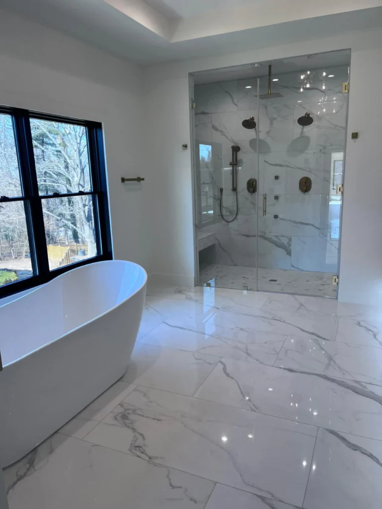 A luxurious, spacious bathroom with a sparkling white freestanding tub, polished marble floor tiles, and a large streak-free glass shower, impeccably cleaned by L&V Cleaning.