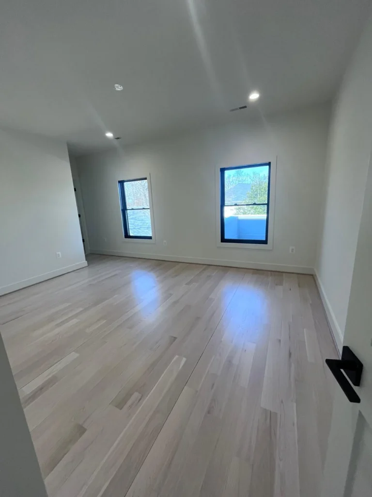An empty, newly built room with gleaming light wood floors, crisp white walls, and clean black-framed windows, showcasing the move-in cleaning services of L&V Cleaning.