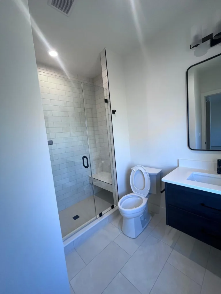 "A bright, spotless bathroom featuring a white bathtub, grey textured shower tiles, matte black hardware, and a clean dark vanity, maintained by L&V Cleaning.
