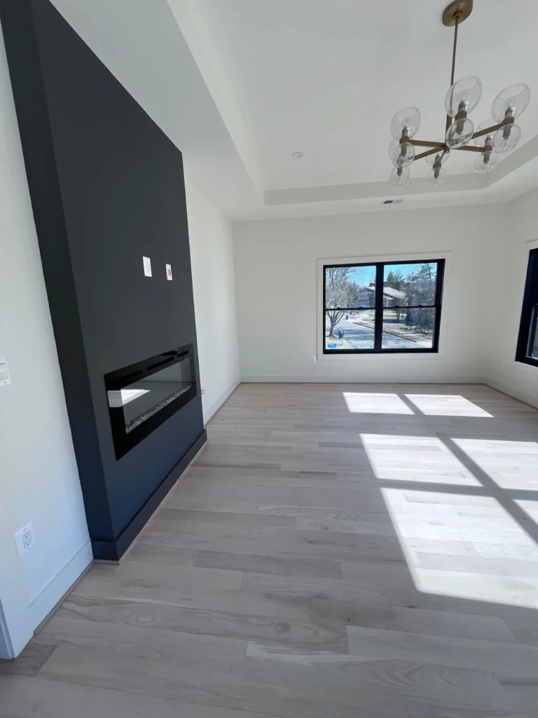 A sunlit, empty living space with freshly swept light wood floors and a sleek black modern fireplace, showcasing move-in ready cleaning results by L&V Cleaning