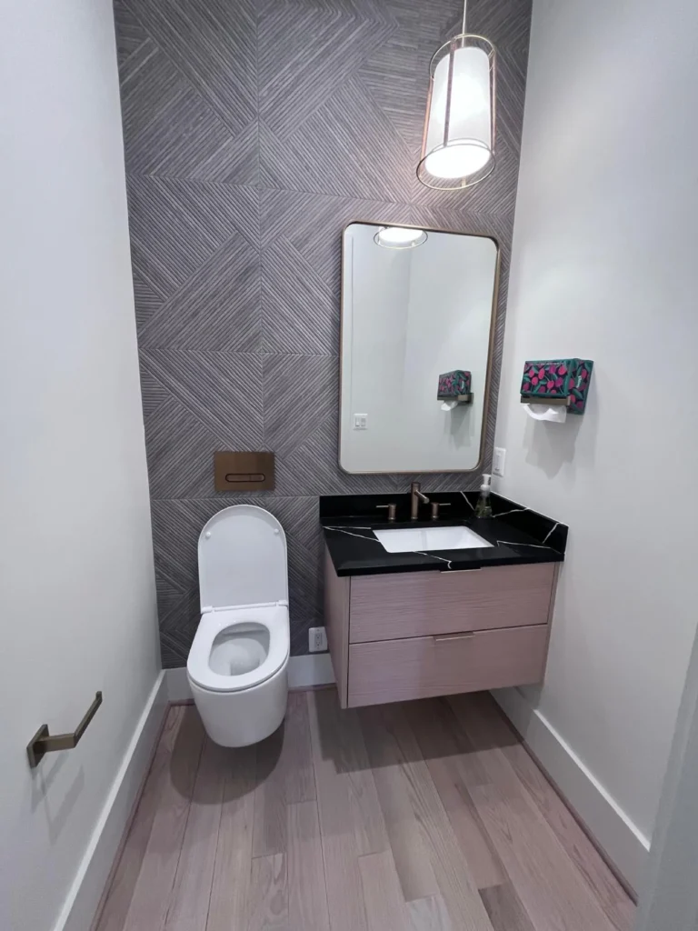 A pristine modern powder room featuring textured grey wallpaper, a sleek floating vanity with a black countertop, and a streak-free mirror, maintained by L&V Cleaning.