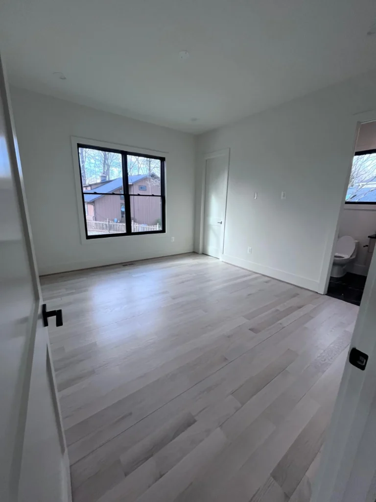 A bright, empty bedroom with freshly swept light wood floors and clean black-framed windows, ready for move-in after a deep clean by L&V Cleaning.