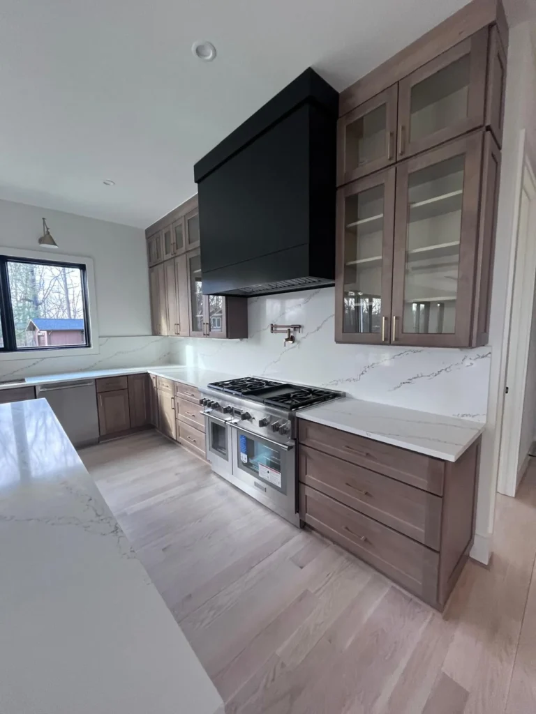 A beautiful, newly cleaned kitchen featuring natural wood cabinets, gleaming marble countertops, a large black range hood, and spotless stainless steel appliances by L&V Cleaning.