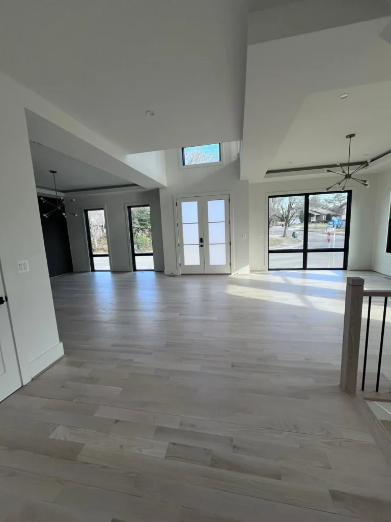 A wide view of a bright, sunlit open-concept living area with immaculate light wood floors and clean, streak-free windows, showing a thorough move-in clean by L&V Cleaning.
