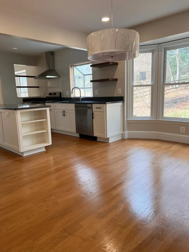 An open-concept kitchen with highly polished hardwood floors and wiped-down white cabinets, cleaned by L&V Cleaning.