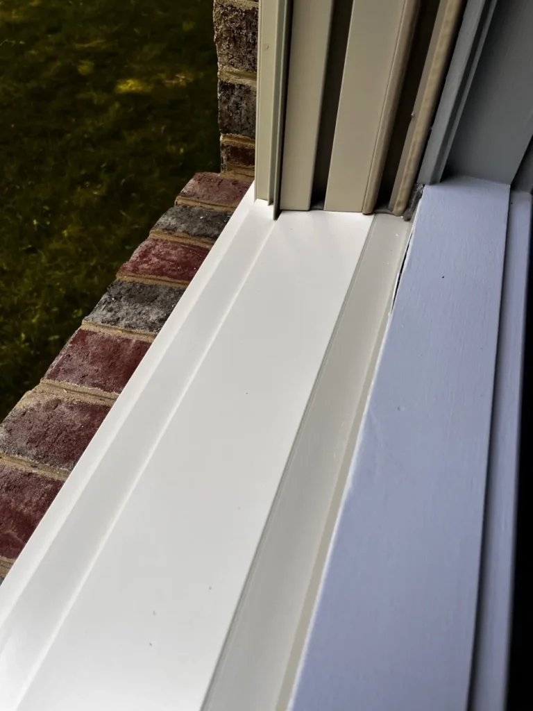 Close-up detail of a thoroughly cleaned white window sill and exterior frame against a red brick wall by L&V Cleaning.