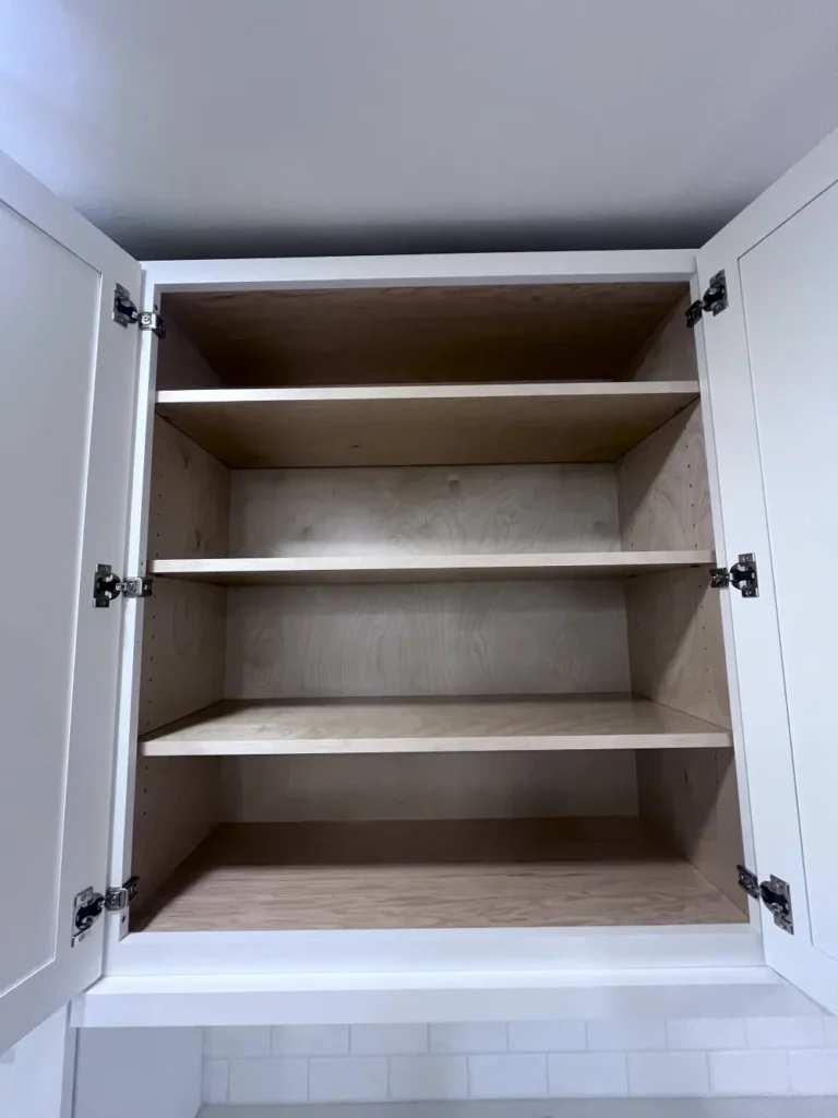 An open, empty white kitchen cabinet with deeply cleaned wooden shelves, demonstrating interior cabinet cleaning by L&V Cleaning.