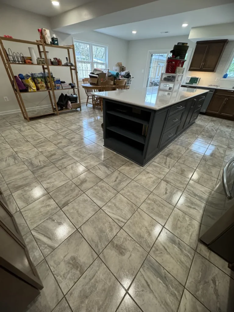 A wide view of a kitchen and dining area featuring freshly mopped glossy square tile flooring and a wiped-down center island by L&V Cleaning.