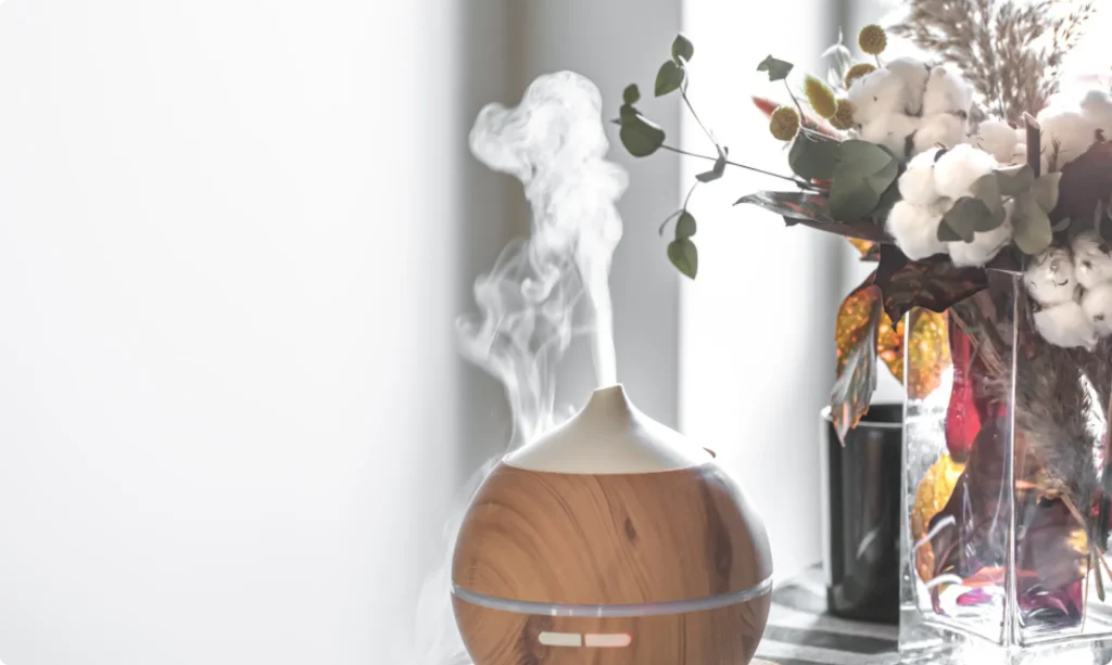 A wood-grain essential oil diffuser releasing mist next to a floral arrangement, featured in a blog post about natural home air fresheners by L&V Cleaning