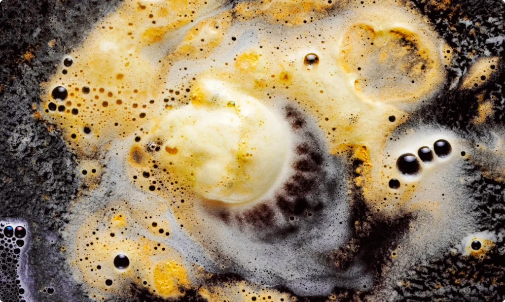 A close-up of foamy cleaning solution breaking down stubborn grease on a dark surface, demonstrating safe methods to clean kitchen cabinets without causing damage.