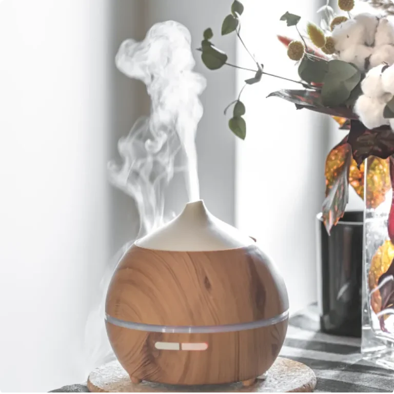 A wood-grain essential oil diffuser releasing mist next to a floral arrangement, featured in a blog post about natural home air fresheners by L&V Cleaning