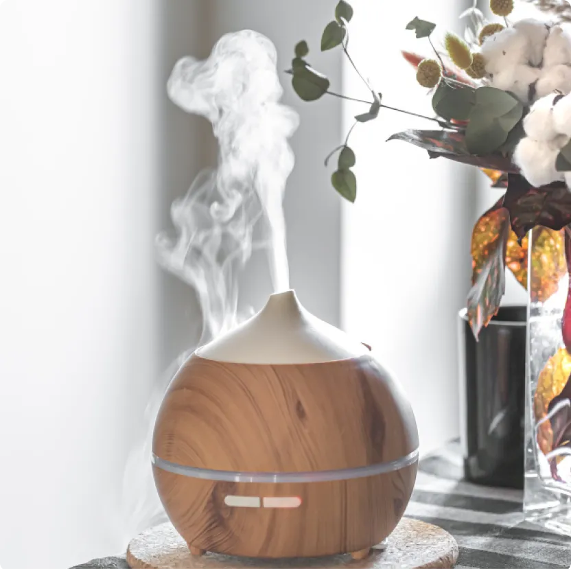 A wood-grain essential oil diffuser releasing mist next to a floral arrangement, featured in a blog post about natural home air fresheners by L&V Cleaning