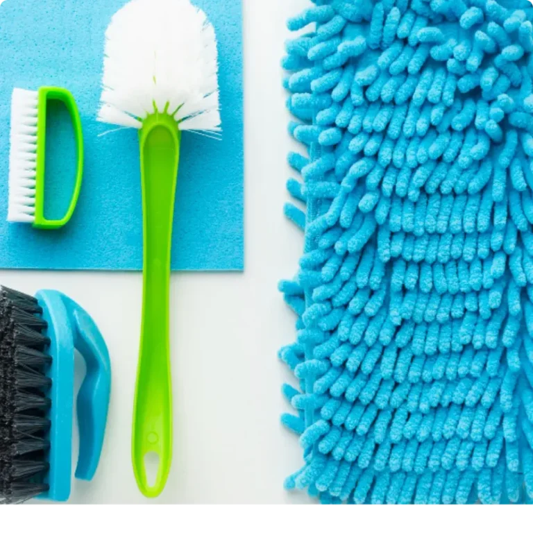 An flat lay arrangement of essential home cleaning supplies including a white spray bottle, blue microfiber cloth, green and black scrubbing brushes, and a fluffy blue duster, matching the recommended tools for Northern Virginia homeowners.