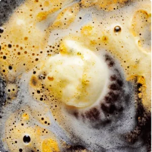 A close-up of foamy cleaning solution breaking down stubborn grease on a dark surface, demonstrating safe methods to clean kitchen cabinets without causing damage.