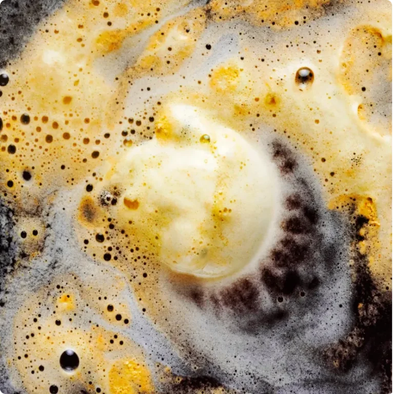 A close-up of foamy cleaning solution breaking down stubborn grease on a dark surface, demonstrating safe methods to clean kitchen cabinets without causing damage.