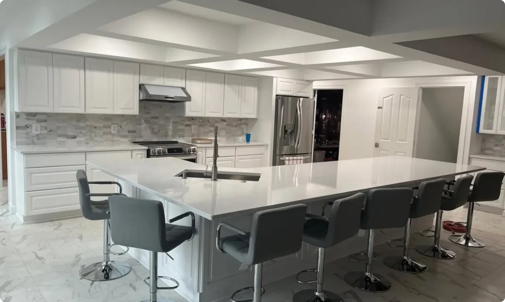 Spotless modern kitchen featuring polished white quartz countertops, white cabinetry, marble tile flooring, stainless steel appliances, and a large island lined with grey barstools cleaned by L&V Cleaning.