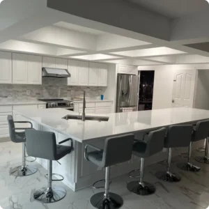 Spotless modern kitchen featuring polished white quartz countertops, white cabinetry, marble tile flooring, stainless steel appliances, and a large island lined with grey barstools.