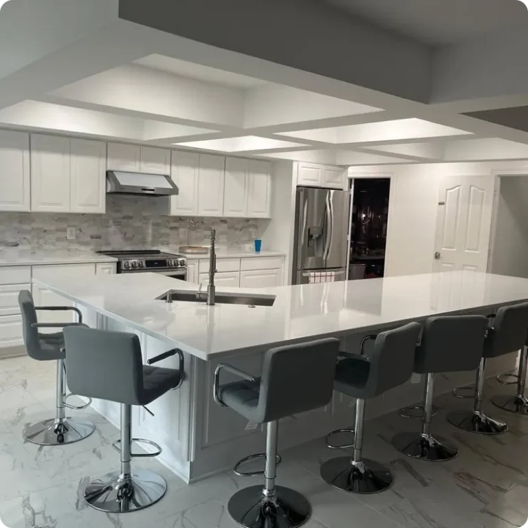 Spotless modern kitchen featuring polished white quartz countertops, white cabinetry, marble tile flooring, stainless steel appliances, and a large island lined with grey barstools.